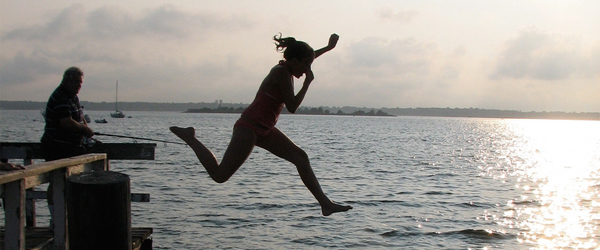A silhouetted girl jumps off a pier