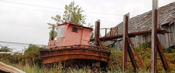 A rusty boat sits adjacent to a weathered wooden structure